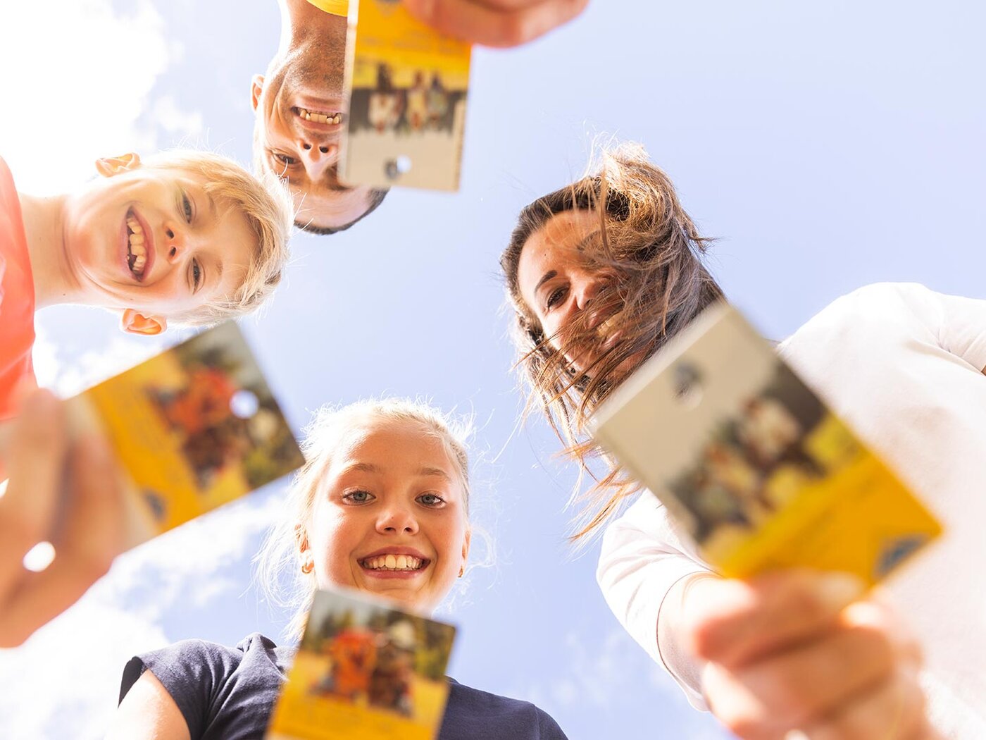 Vier fröhliche Menschen halten die Super.Sommer.Card in die Kamera und blicken lachend aus der Froschperspektive in den Himmel.