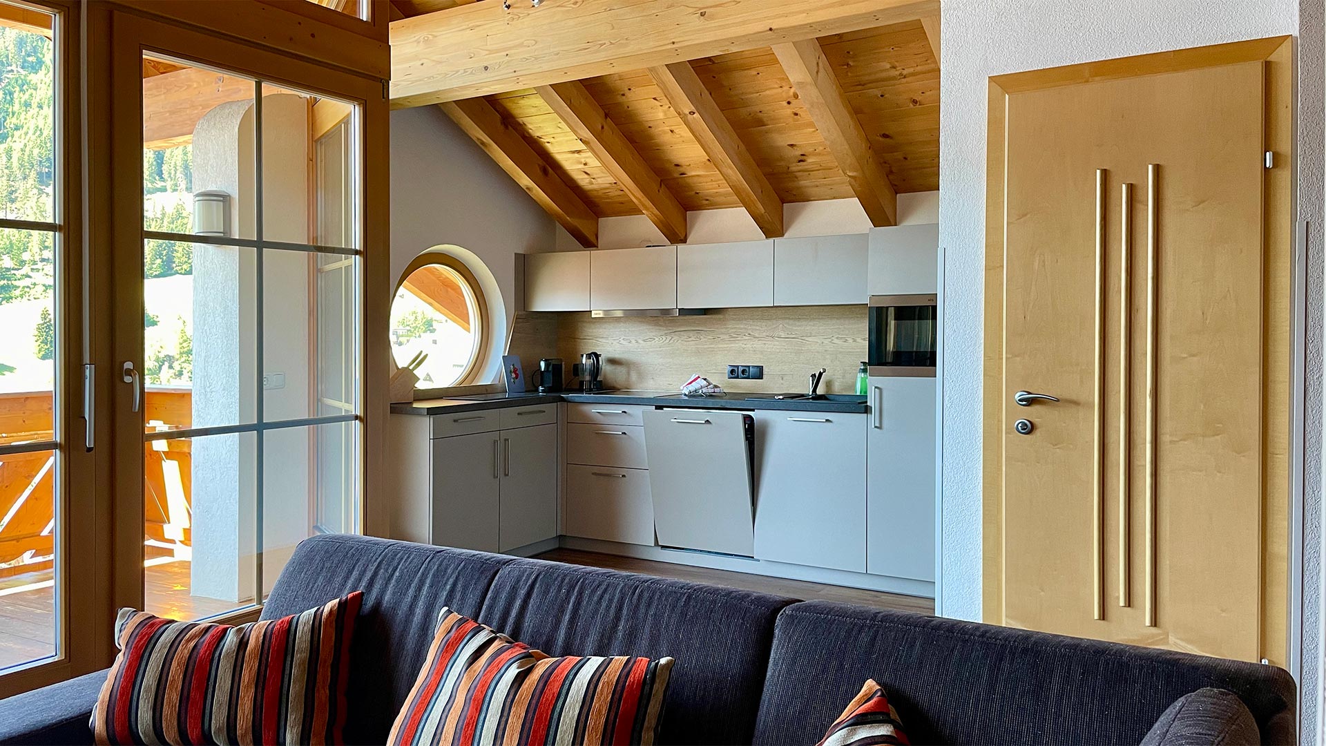 Wohnbereich im Haus Montjola Serfaus mit Küchenzeile, Sofa und Zugang zum Balkon.