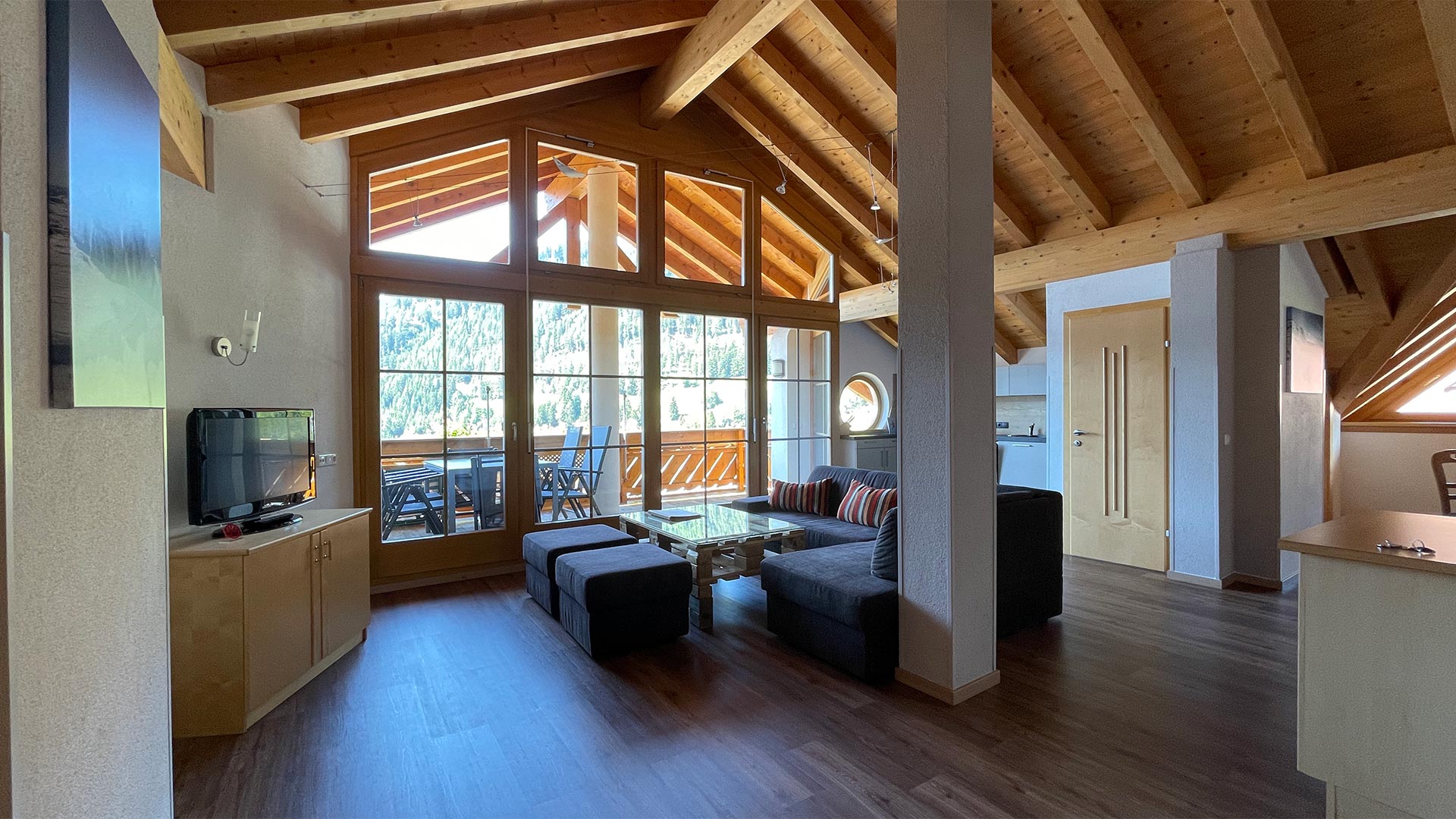 Wohnbereich im Haus Montjola Serfaus mit Sofa, Holzdecke und großen Panoramafenstern.