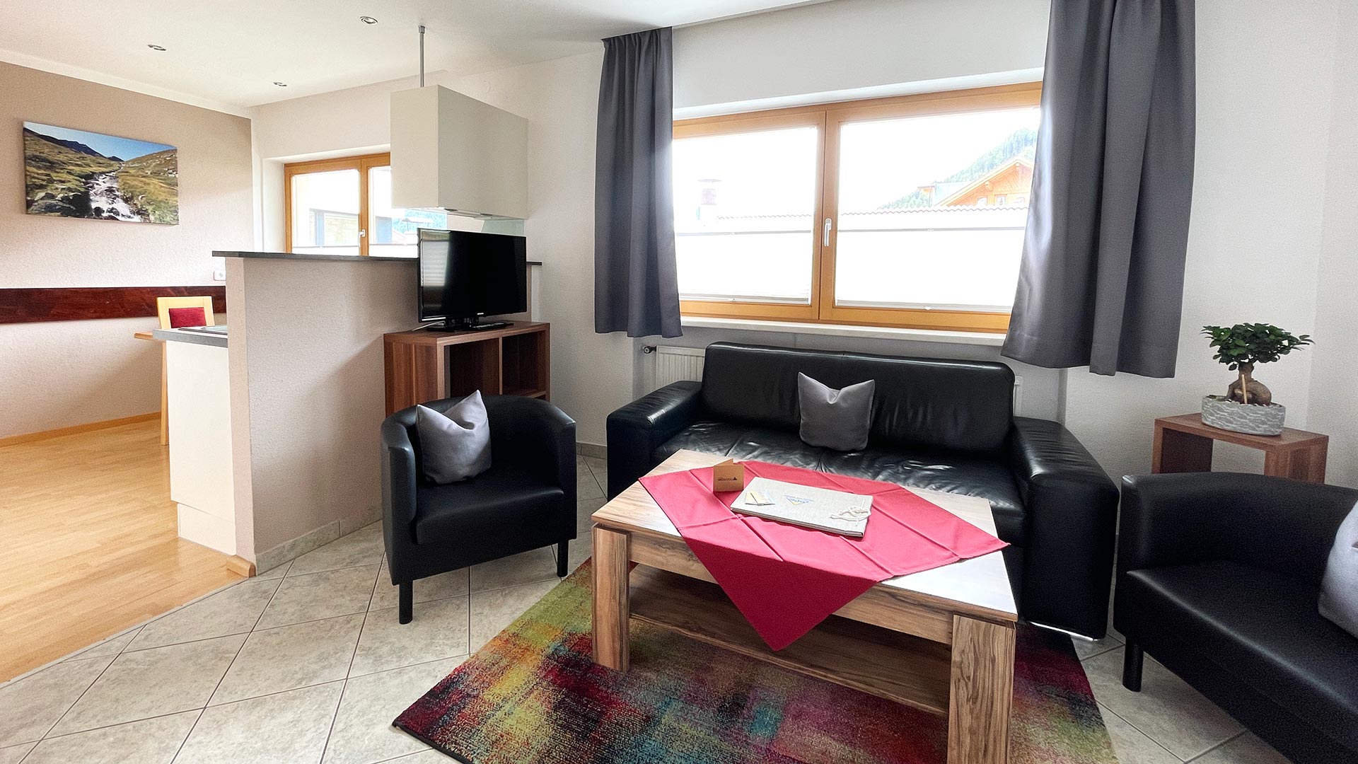 Wohnbereich im Haus Montjola Serfaus mit Sofa, Esstisch, Küche und großem Fenster.