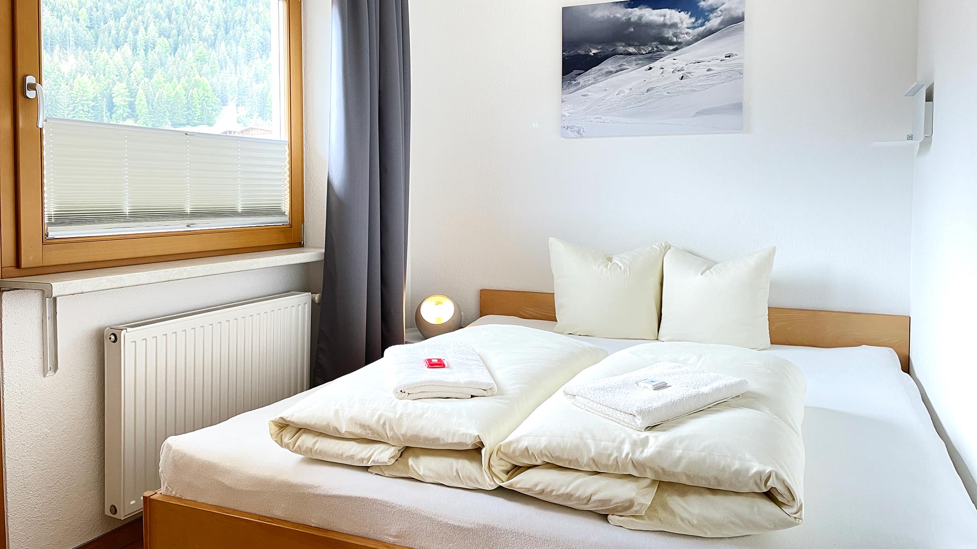 Schlafzimmer im Haus Montjola Serfaus mit Doppelbett, Fenster und hellen Holzmöbeln.