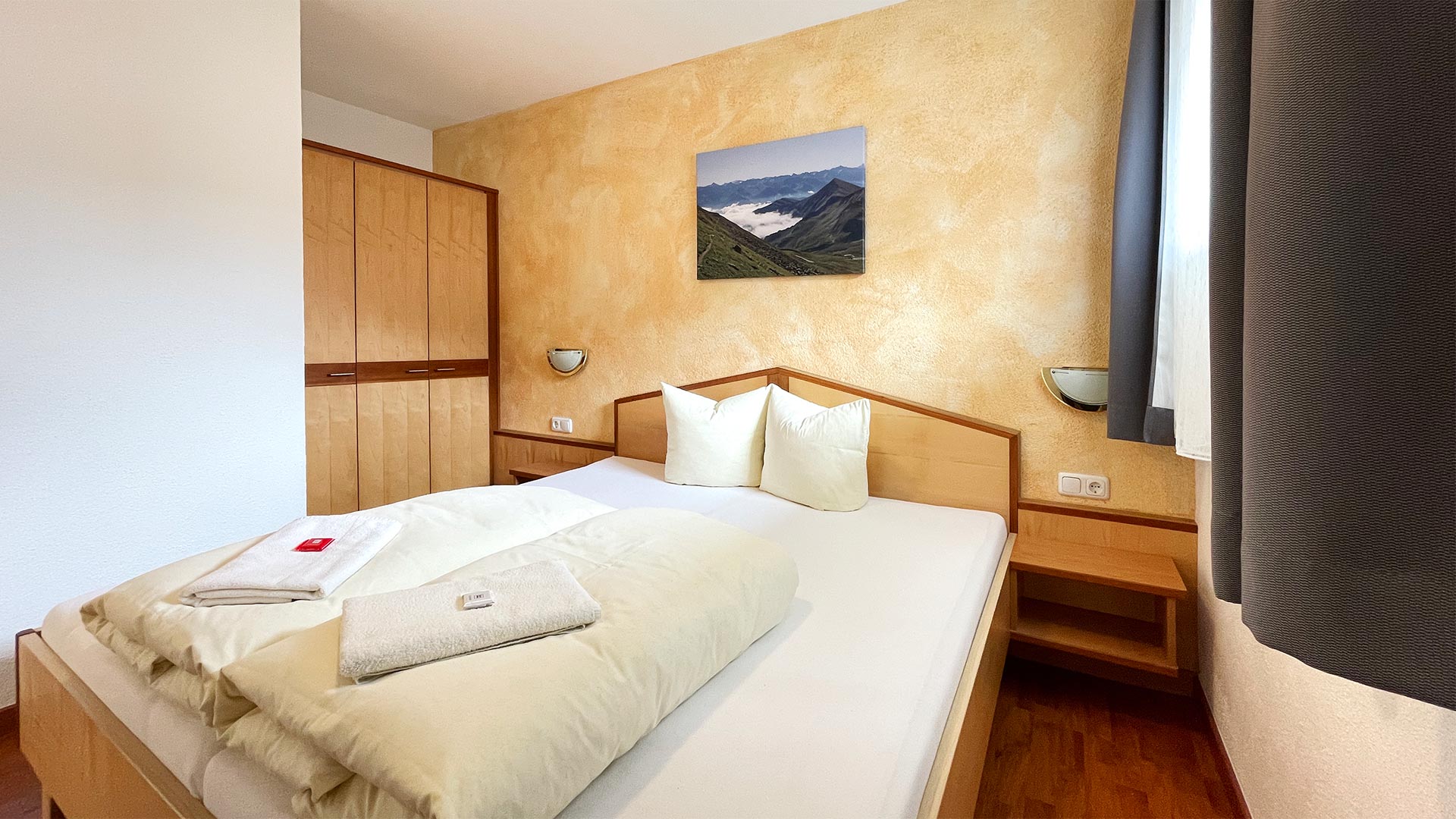 Schlafzimmer im Haus Montjola Serfaus mit Doppelbett, Holzmöbeln und Bergbild.