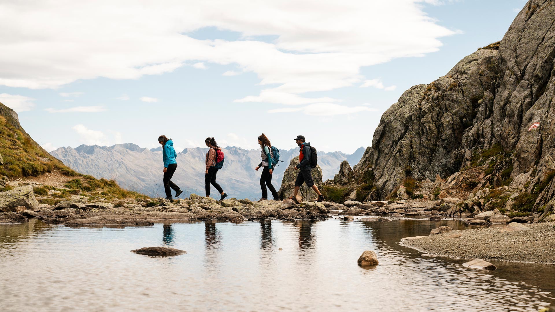 Wandergruppe bei Serfaus überquert einen Bach in felsiger Berglandschaft.