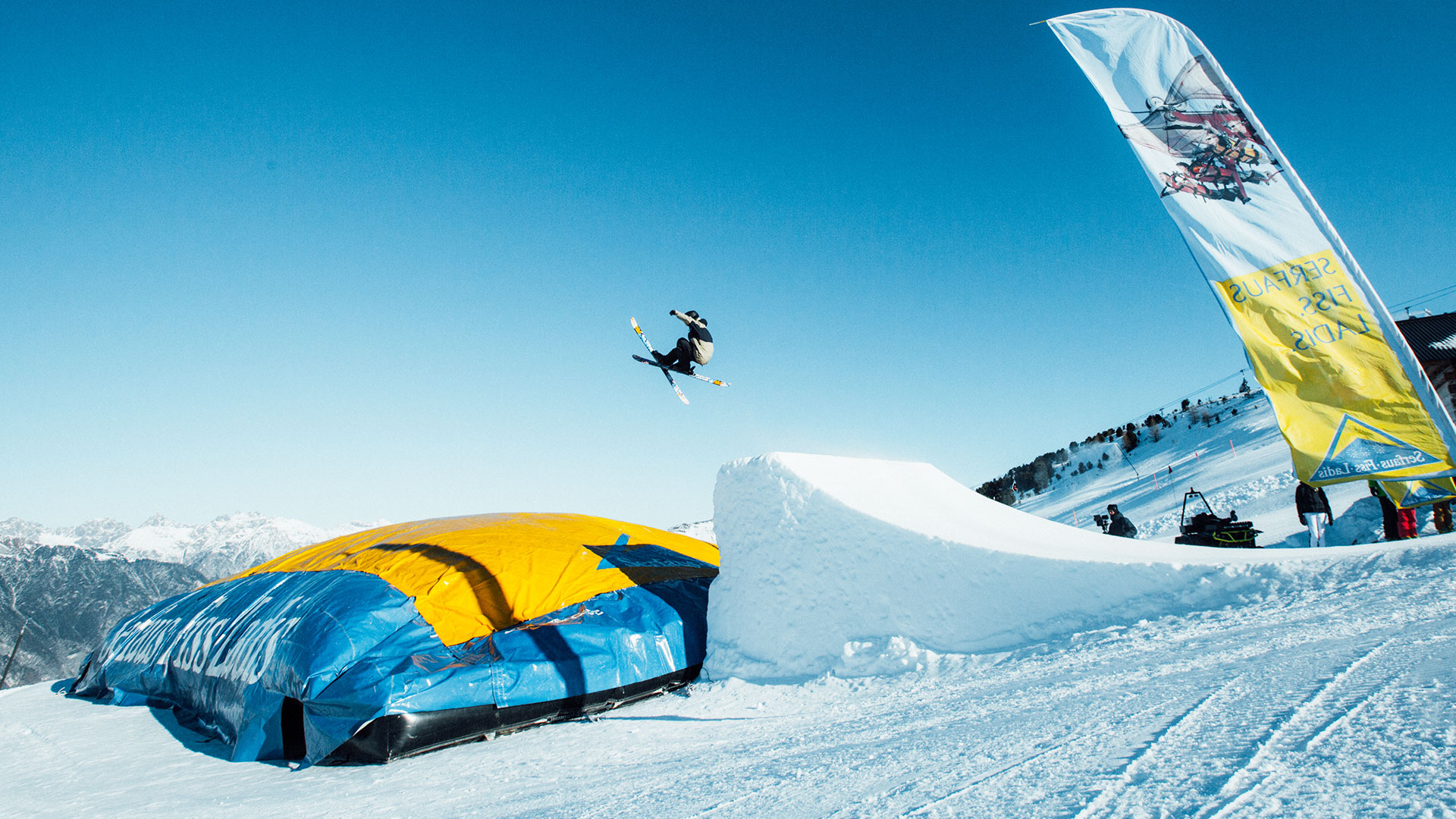 Skifahrer springt im Snowpark Fiss hoch über Schanze mit Airbag und blauem Himmel im Hintergrund.